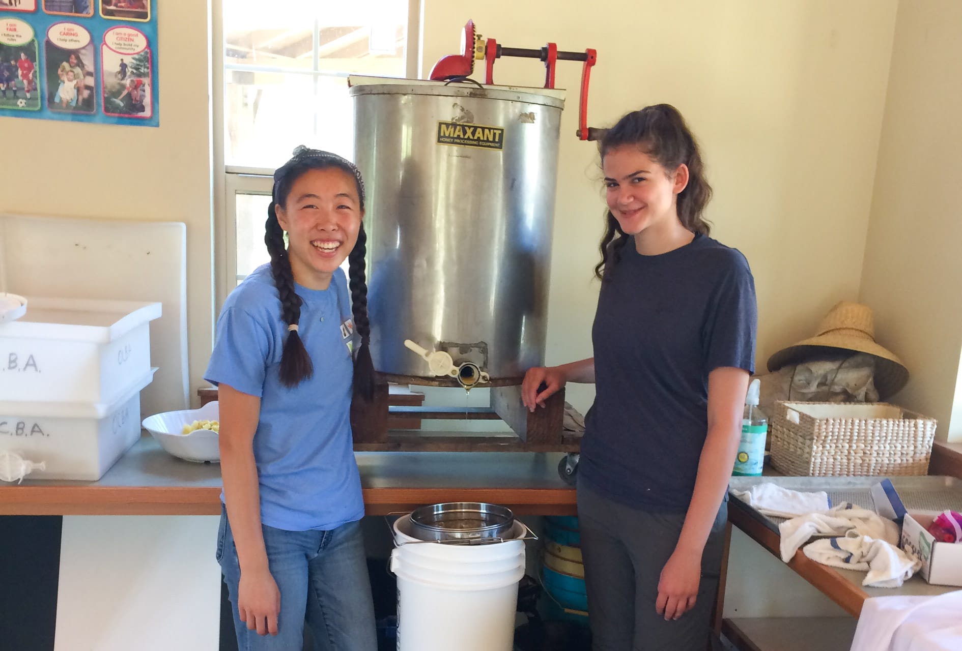 Two female teens standing next to a honey vat